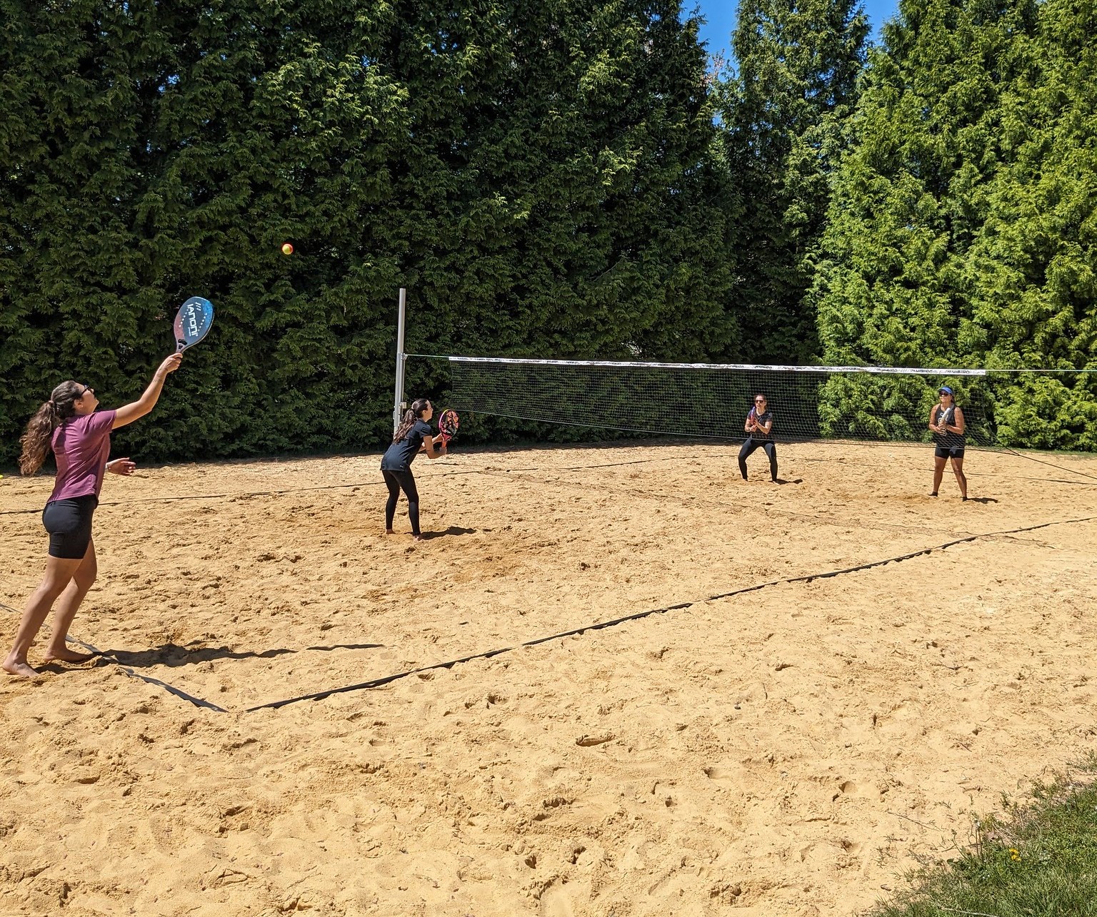 Four adults play beach tennis