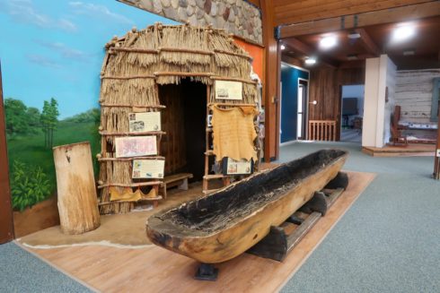 Legacy of the People exhibit with a hut made of straw and branches and a handmade canoe.