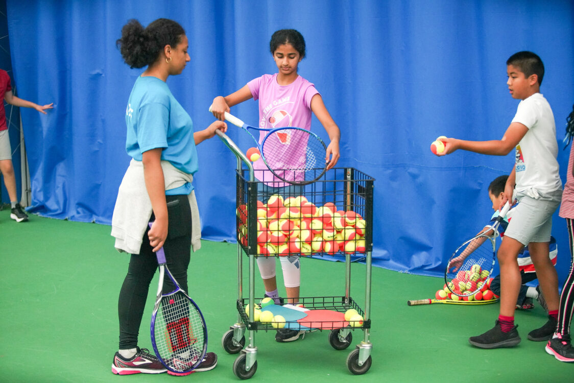 instructor and students picking up tennis ball at summer camp