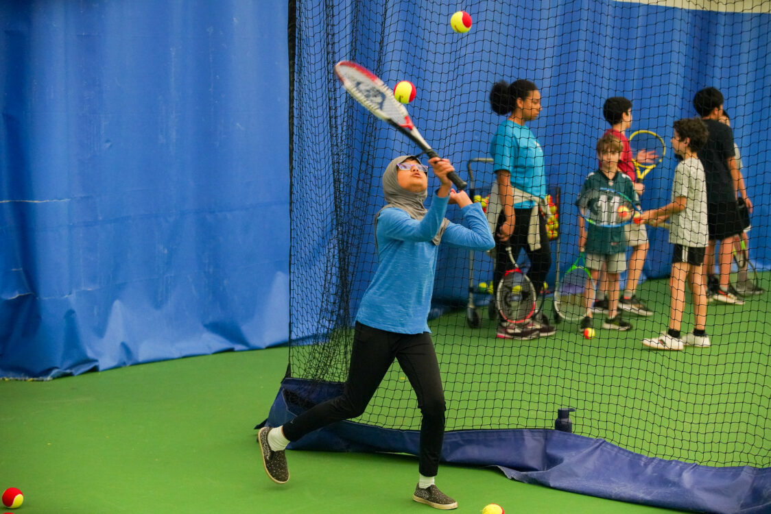 camper serving in tennis at indoor tennis summer camp