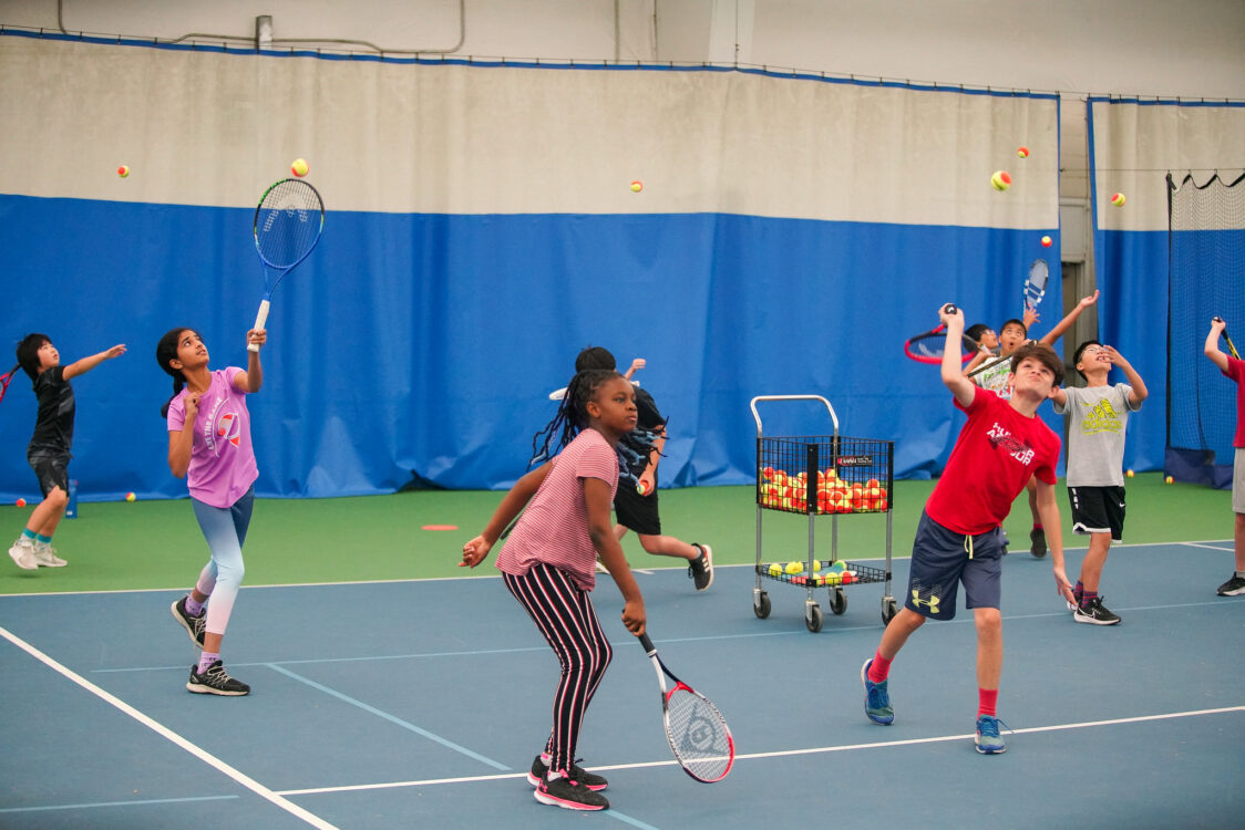 a bunch of campers practicing their tennis serve at tennis summer camp