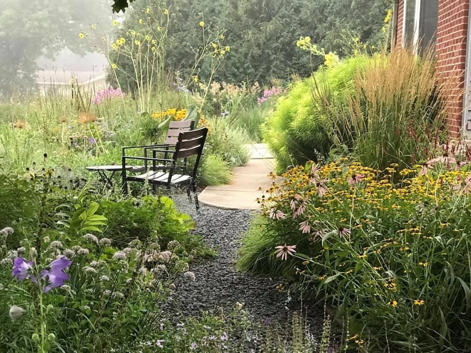 Empty chair in the middle of a home garden outside with perennial flowers and grasses.