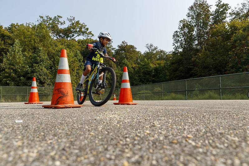 A youth on a bike rides between orange cones