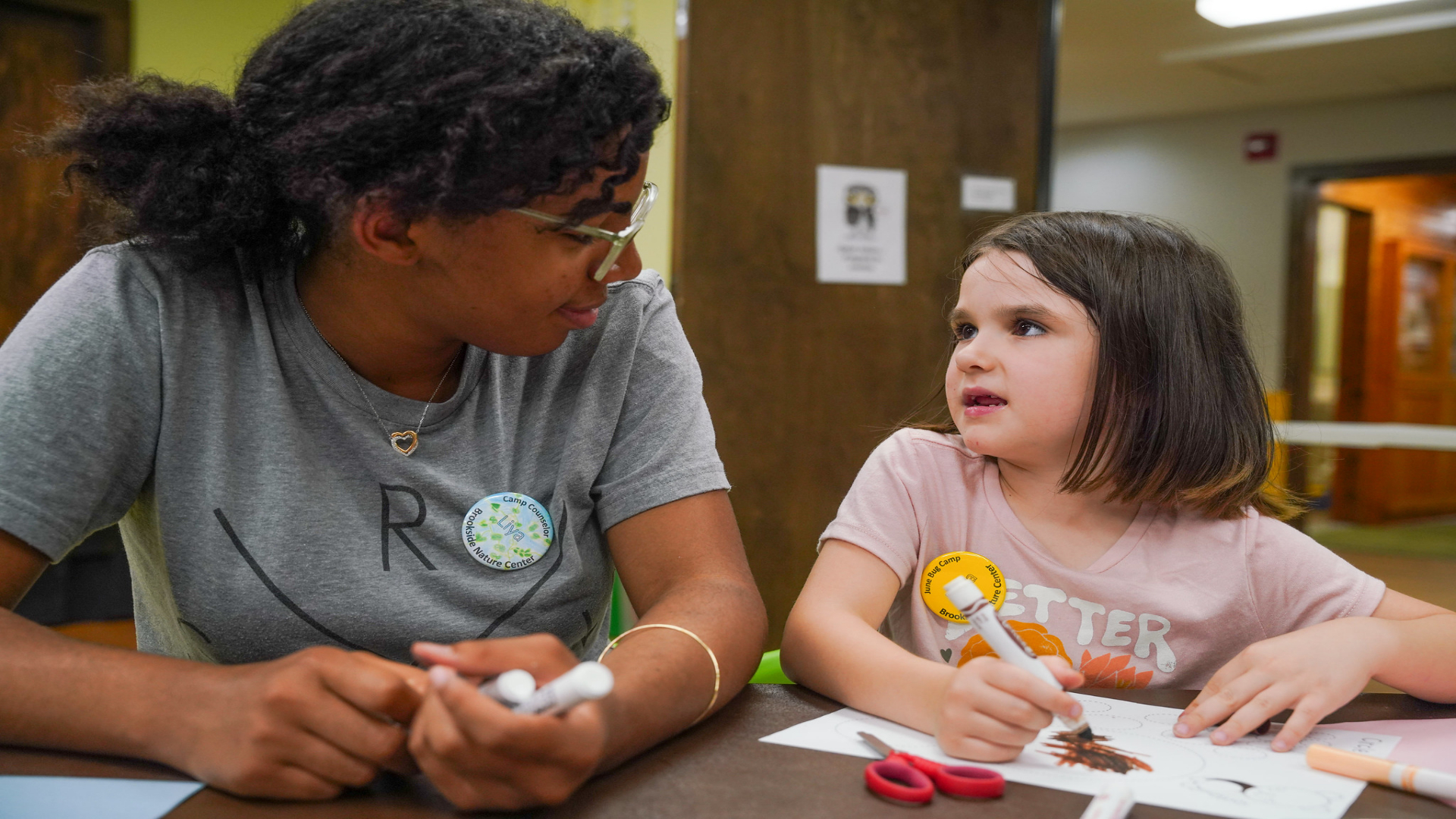 A volunteer camp counselor helps a young camper with an art project.