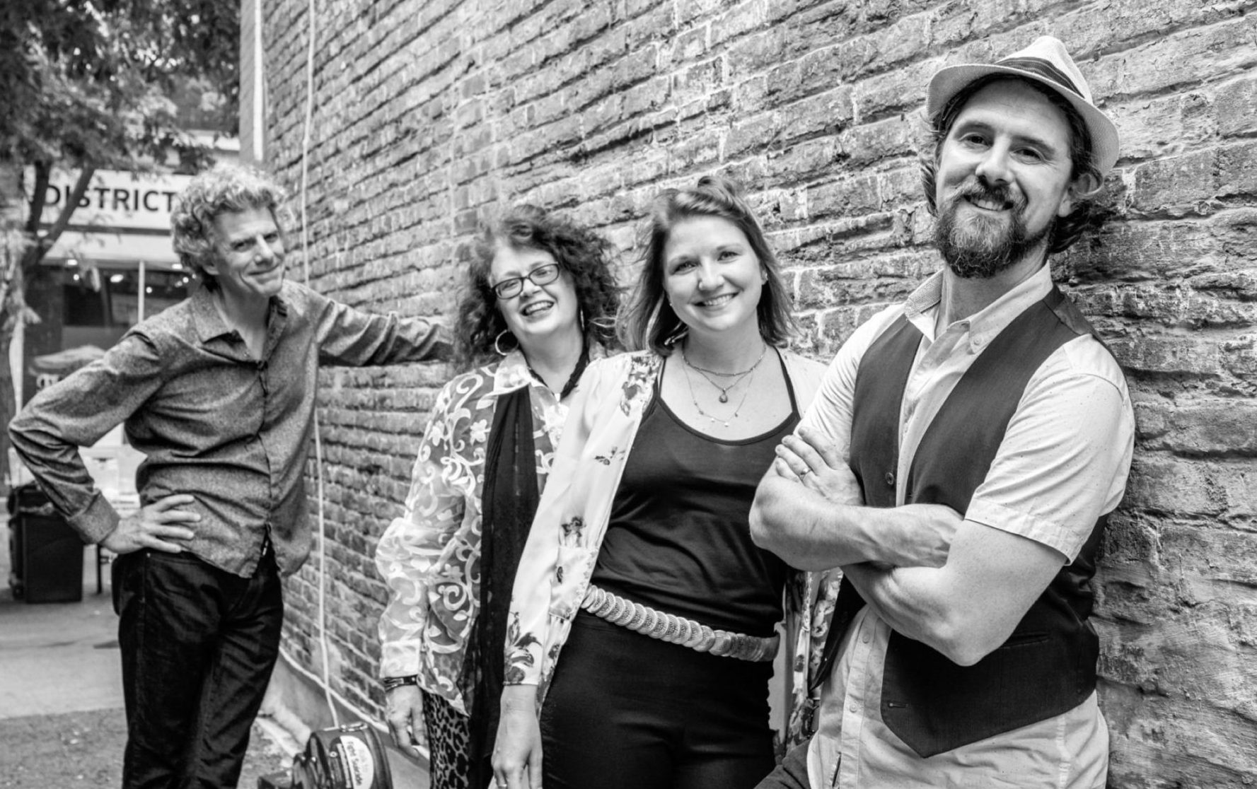 black and white photo of band members leaning against a brick wall outdoors