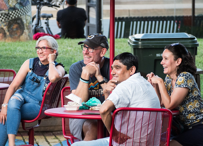 friends seated at table looking toward stage and laughing