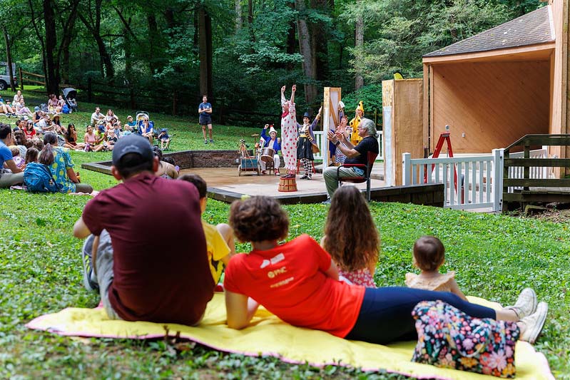 family lying in the grass watching performance at Happenstance Theater in summer 2023