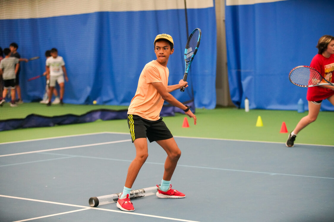 teen getting ready to hit the tennis ball at summer camp